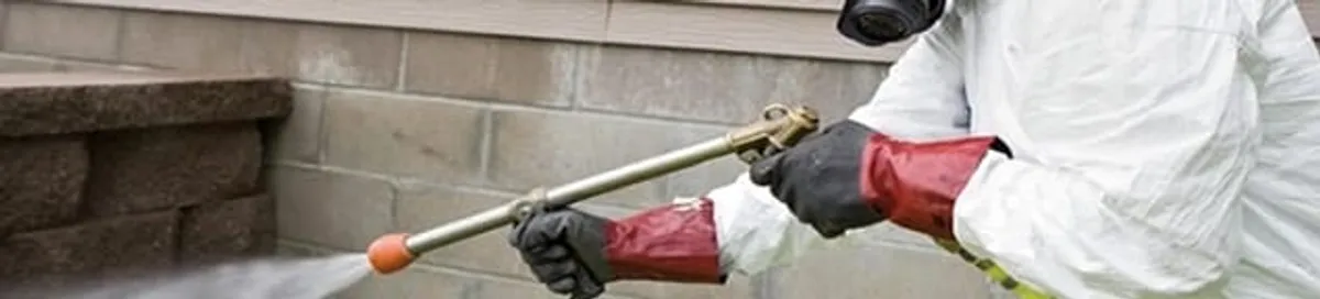 Pest control technician applying exterior insect treatment along a home foundation in Spokane, WA