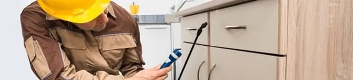Roach exterminator applying treatment under kitchen cabinets in Spokane, WA