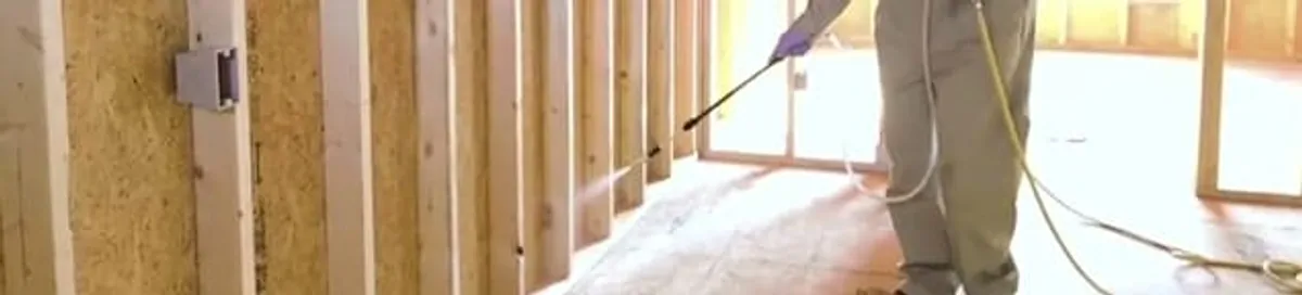 Termite treatment technician applying spray along framing and unfinished walls in Spokane, WA